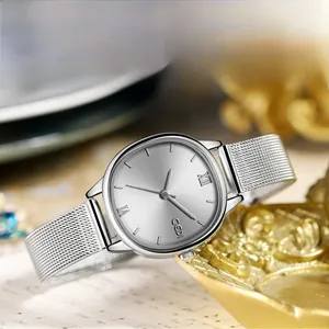 Elegant oval dial watch with silver Milanese mesh strap displayed on a gold tray