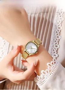 Close-up of golden oval watch with pearl dial and mesh strap on a female wrist