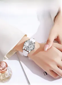 Close-up of a luxury women's silver watch with a white strap and date window on a wrist