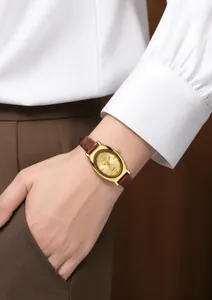 Close-up of golden oval quartz watch with brown leather strap worn on wrist