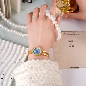 Montre dorée élégante avec cadran bleu dégradé et cristaux portée au poignet d'une femme
