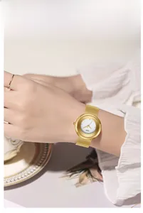 Close-up of gold mesh band watch with minimalist white dial and diamond markers