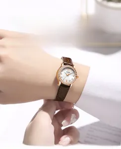 Detail of a rose gold lady watch with diamond bezel and brown leather strap on wrist