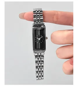 Detailed macro view of a rectangular black dial watch with silver steel band on a model hand