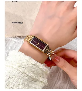 Close-up of rectangular gold watch with burgundy dial and stainless steel mesh strap