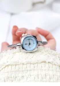 Detailed close-up of a silver braided cuff watch with a light blue square sunray dial