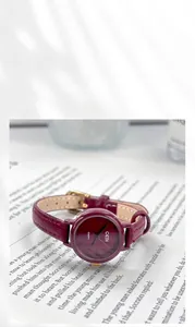 Close-up of GEDI quartz watch with wine red leather strap and gold bezel on a book