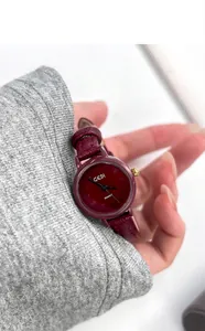 Close-up of a burgundy leather quartz watch with gold bezel on a woman's wrist