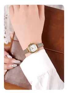Gros plan d'une montre vintage carrée avec boîtier doré et bracelet en cuir gris au poignet