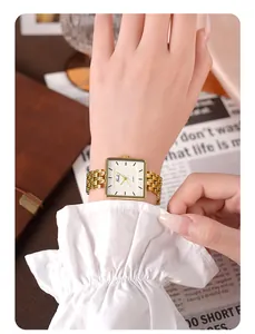Détail d'une montre carrée dorée pour femme avec bracelet maillé sur fond de bureau