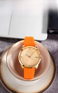 Close-up of GEDI watch with orange silicone strap and gold dial on a ceramic cup
