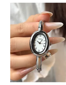 Detalle de reloj plateado ovalado con números romanos y brazalete rígido para mujer