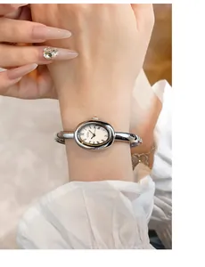 Detalle de reloj ovalado plateado con números romanos y brazalete rígido en la muñeca