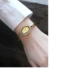 Detailansicht einer ovalen champagnergoldenen Uhr mit Strasssteinen am Handgelenk