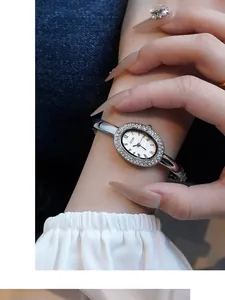 Nahaufnahme einer silbernen Oval-Uhr mit Strass-Lünette und römischen Ziffern am Handgelenk