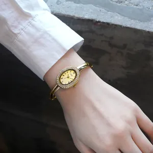 Montre bracelet ovale dorée pour femme avec lunette en cristal et chiffres romains