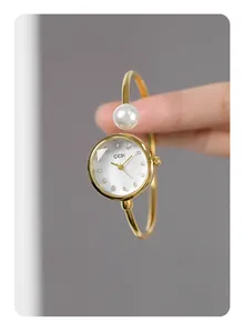 Dettaglio dell'orologio a bracciale dorato con quadrante in madreperla e perla bianca