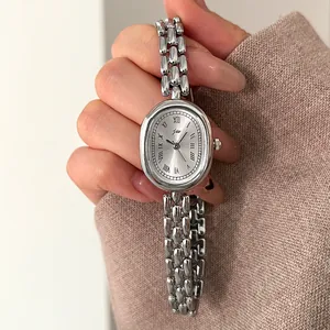 Detail of silver oval vintage watch with roman numerals and metallic chain bracelet