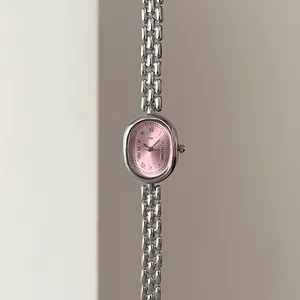 Detailed macro view of an oval pink watch dial with Roman numerals and silver metal strap