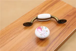 Detail of vintage bronze ceramic cabinet handle and pink rose floral knob on wood board
