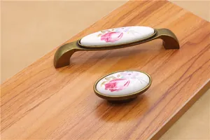 Close-up of white ceramic cabinet handles with pink floral patterns and bronze base