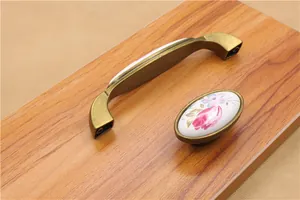 Detail of vintage bronze ceramic handles with pink floral patterns on wood surface