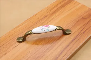 Detail of floral ceramic furniture handle with antique bronze finish on wood