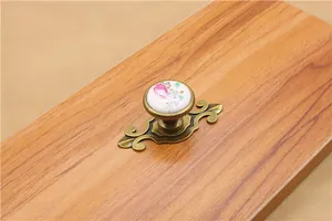 Detail of floral ceramic drawer knob with antique bronze base on a wooden surface