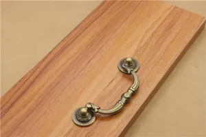 Close-up of antique bronze drawer handle with floral engraving on a wooden surface