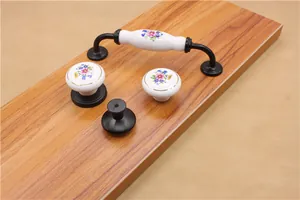 Detail view of floral ceramic cabinet handles and matte black knobs on a wood surface