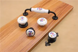 Detailed view of ceramic floral cabinet knobs and handles with black metal bases on wood