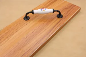Detail of floral ceramic and black metal drawer handle on wood cabinet door