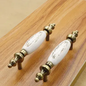 Detail of white ceramic cabinet handles with gold scroll patterns and bronze metal ends