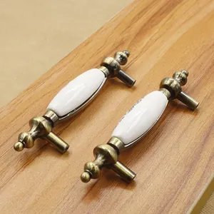 Antique brass and white ceramic cabinet handles with floral patterns on wood background