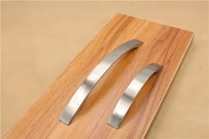 Close-up of curved brushed aluminum handles in two sizes on a wooden drawer surface