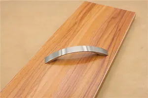 Macro shot of curved silver brushed aluminum handle installed on a wooden furniture panel