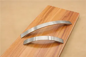 Close-up of brushed silver curved furniture handles in two lengths on wood surface