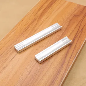 Close-up of brushed silver aluminum furniture handles in two lengths on wood surface