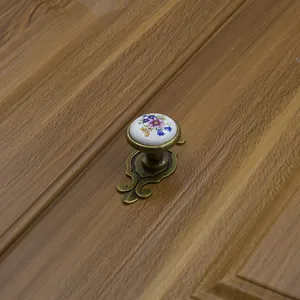 Detail of floral ceramic cabinet handle with antique bronze base on dark wood drawer