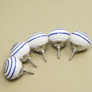 Five white ceramic cabinet knobs with blue stripes and silver hardware on beige leather