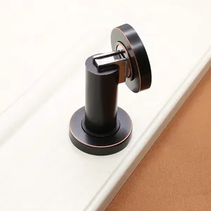 Detail view of a matte black and bronze zinc alloy magnetic door stopper on wood