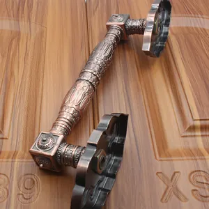 Detail of red antique bronze door handle with ornate floral carvings on a wooden door