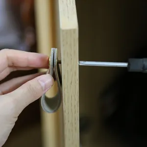 Detail of beige leather loop handle being installed on a wooden cabinet with brass screw