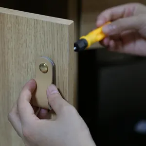 Detailed view of beige leather drawer pull being installed on a light wood cabinet door