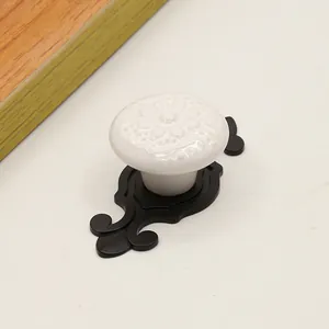 Close-up of white ceramic cabinet knob with floral relief and vintage black metal base