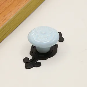 Detailed view of light blue ceramic drawer handle with floral relief and black base