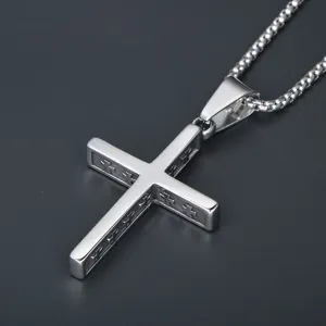 Macro shot of silver cross pendant showing detailed embossed reliefs on a steel box chain