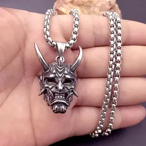 Detalle del colgante de máscara de demonio gótico en una cadena de bolas sostenida a mano