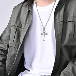Close-up of a silver Ankh cross pendant on a thin chain worn over a white T-shirt