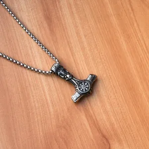 Detailed close-up of Viking Mjölnir pendant with skull and Vegvísir on wooden background